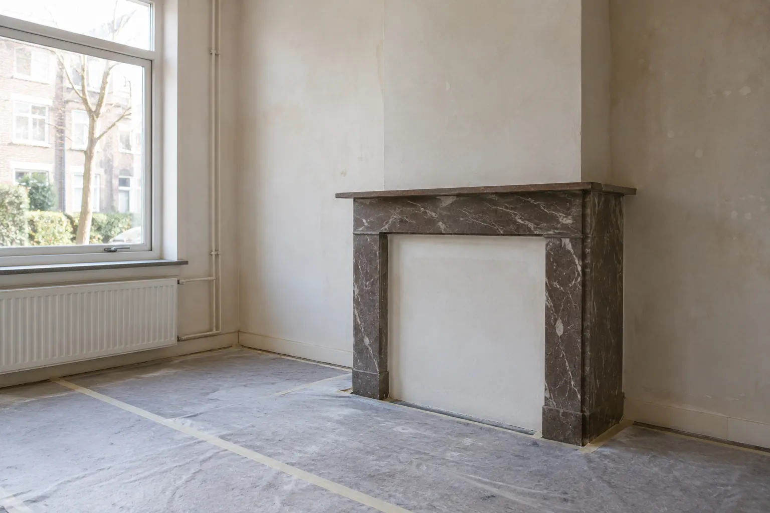 Lege kamer met afgedekte vloer en een donkere schouw met marmerlook tegen een lichte muur — illustratief beeld